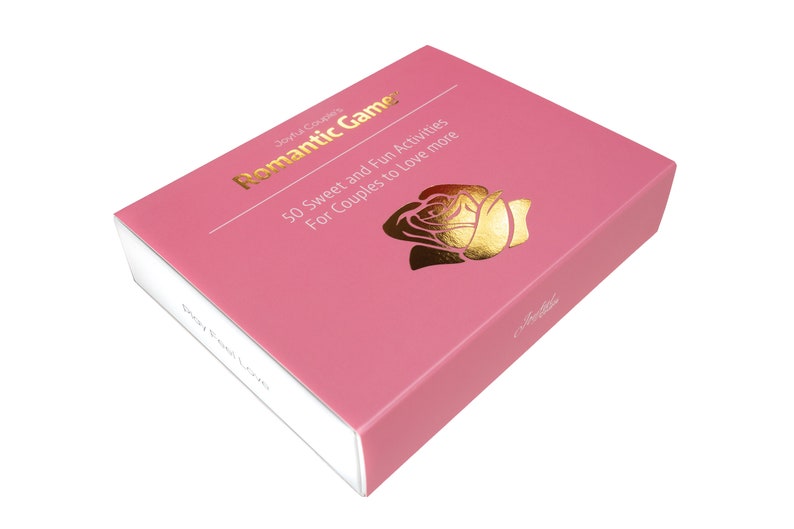 Puede incluir: Una caja rosa con el t&iacute;tulo "Romantic Games" en letras doradas y una ilustraci&oacute;n de rosa dorada. La caja contiene "50 actividades dulces y divertidas para que las parejas amen m&aacute;s". La caja est&aacute; en &aacute;ngulo sobre un fondo blanco.