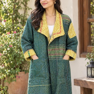May include: A long-sleeved jacket featuring a dark green quilted fabric with a textured pattern. The garment includes a wide, folded collar and cuffs in a contrasting mustard yellow fabric with a subtle print, and two large front pockets.