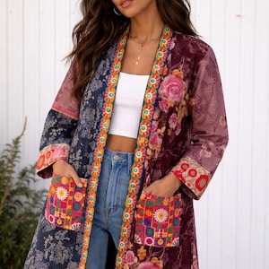 Può includere: Una giacca lunga e fantasia con un design floreale. La giacca presenta un mix di colori, tra cui blu navy, bordeaux e rosa, con dettagli ricamati e tasche. La giacca è indossata aperta, mostrando un top bianco e jeans blu.