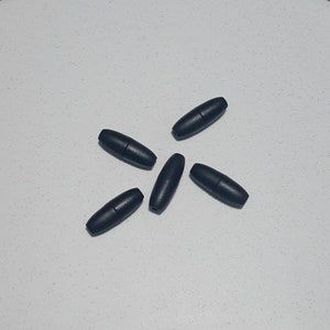 May include: Five black plastic cord end stoppers, also known as cord locks, are arranged in a star shape on a white surface.
