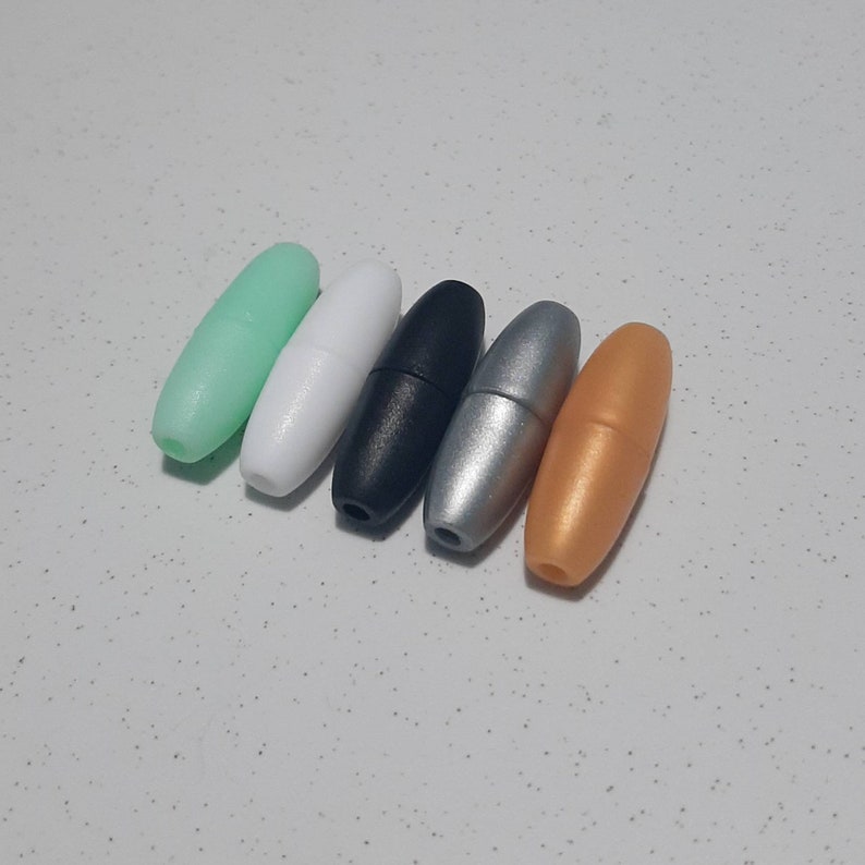 May include: Five plastic cord end stoppers in different colours: mint green, white, black, silver, and gold.