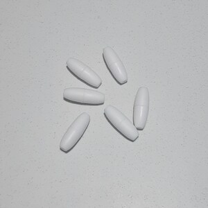 May include: Six white oval-shaped beads, arranged in a starburst pattern on a white surface.