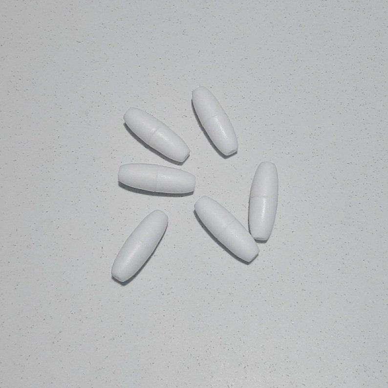 May include: Six white oval-shaped beads, arranged in a starburst pattern on a white surface.