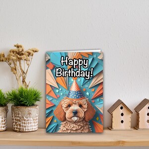 Peut inclure: Une carte d'anniversaire avec un adorable chien brun et blanc portant un chapeau de fête coloré. La carte a un fond bleu avec des découpes de papier orange et bleu et le texte "Happy Birthday!" en noir.