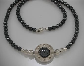 Pode incluir: Um colar de contas de hematita preta com um pingente de prata que apresenta uma pedra redonda preta cercada por um design circular.