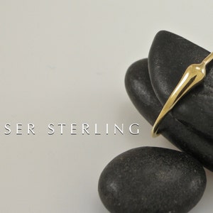 Puede incluir: Un anillo de oro con un dise&ntilde;o abstracto &uacute;nico. El anillo est&aacute; apoyado sobre dos piedras lisas negras. KEISER STERLING est&aacute; escrito en blanco debajo del anillo.
