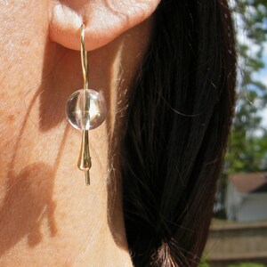 Puede incluir: Pendientes de oro con un cristal redondo transparente. Los pendientes son simples y elegantes.