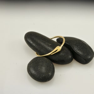 Puede incluir: Un anillo de oro simple con un dise&ntilde;o &uacute;nico ligeramente puntiagudo. El anillo est&aacute; apoyado sobre tres piedras lisas y negras.