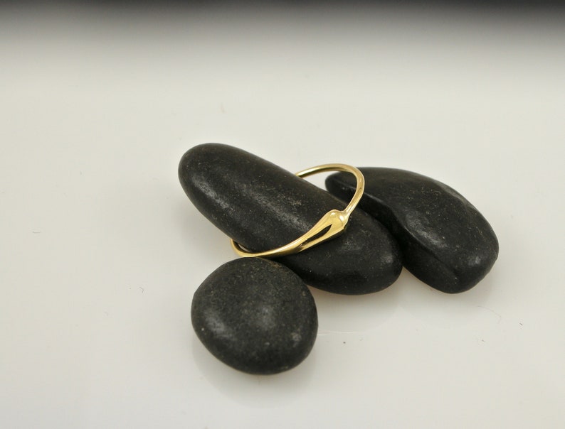 Puede incluir: Un anillo de oro simple con un dise&ntilde;o &uacute;nico ligeramente puntiagudo. El anillo est&aacute; apoyado sobre tres piedras lisas y negras.