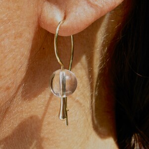 Puede incluir: Pendientes de oro con un colgante de esfera de cristal transparente.