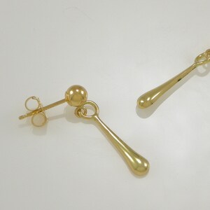 Pode incluir: Um par de brincos de gota de ouro com uma pequena bola no topo e um fecho de poste.