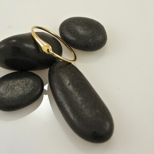 Puede incluir: Un anillo de oro con un dise&ntilde;o liso y redondeado. El anillo est&aacute; apoyado sobre piedras negras.