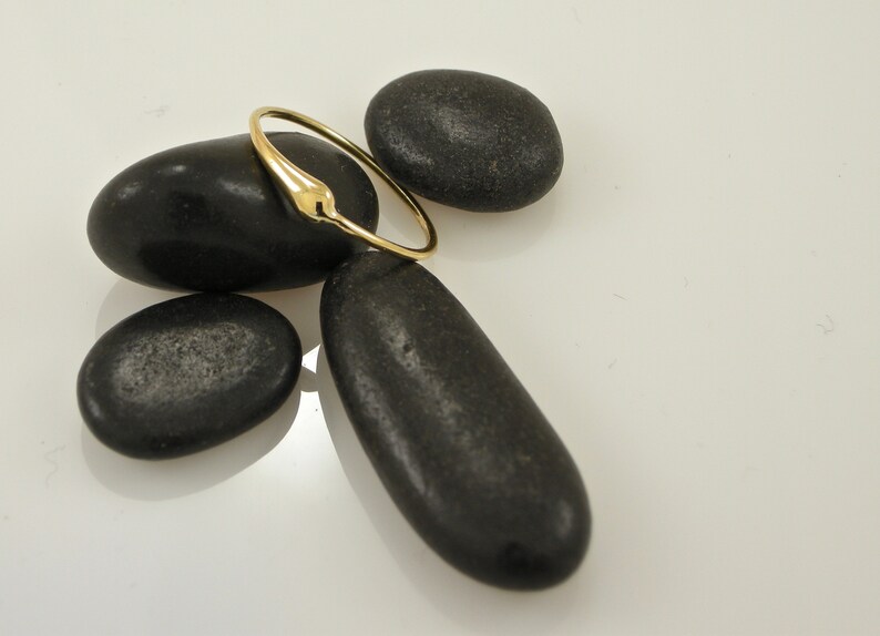 Puede incluir: Un anillo de oro con un dise&ntilde;o liso y redondeado. El anillo est&aacute; apoyado sobre piedras negras.