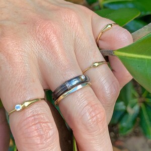 Puede incluir: Una mano con cuatro anillos de oro, uno con un peque&ntilde;o diamante, otro con un diamante m&aacute;s grande y dos bandas simples.