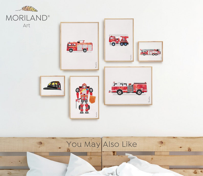 Op de afbeelding: Een set ingelijste prints met rode brandweerauto's, een brandweerhelm en een robot. De prints zijn gerangschikt op een witte muur boven een houten hoofdeinde. De tekst "You May Also Like" is zichtbaar onder de prints.