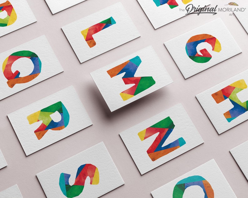 May include: A set of colorful, geometric alphabet letter cards. Each card features a different letter of the alphabet, made up of colorful, geometric shapes. The cards are arranged in a grid pattern on a light pink surface. The text "The Original MORILAND Art" is visible in the top right corner of the image.