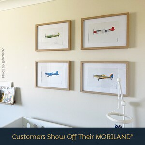 May include: Four framed prints of vintage airplanes, each with a different color scheme, are displayed on a light beige wall. The prints are arranged in a grid pattern, with two prints on the top row and two prints on the bottom row. The prints are all in wooden frames.