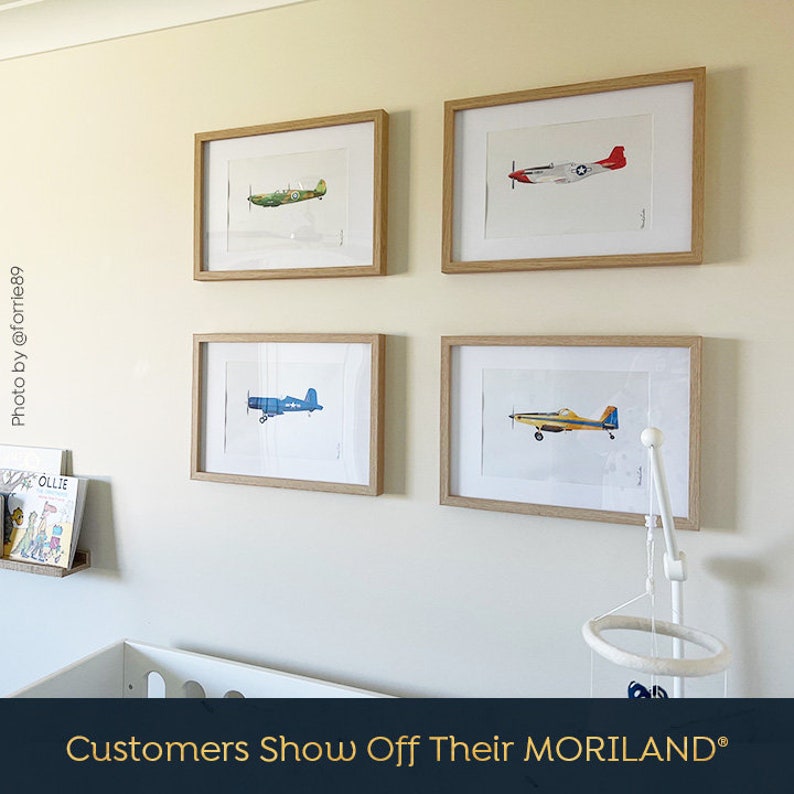 May include: Four framed prints of vintage airplanes, each with a different color scheme, are displayed on a light beige wall. The prints are arranged in a grid pattern, with two prints on the top row and two prints on the bottom row. The prints are all in wooden frames.