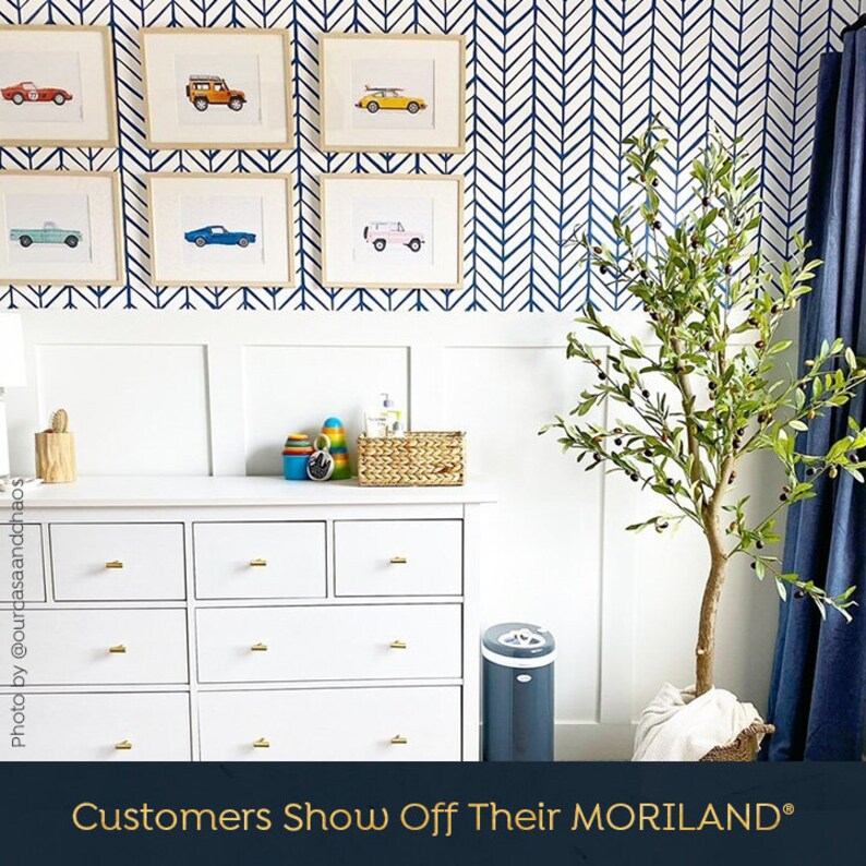 May include: A white dresser with gold drawer pulls, a gray trash can, and a potted olive tree in a white room with blue and white chevron wallpaper. The text "Customers Show Off Their MORILAND&reg;" is at the bottom of the image.