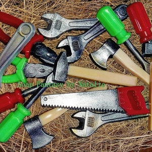 May include: A collection of toy tools made of soap, including a wrench, pliers, a saw, a hammer, an axe, and screwdrivers. The tools are arranged on a bed of straw and have a realistic appearance.