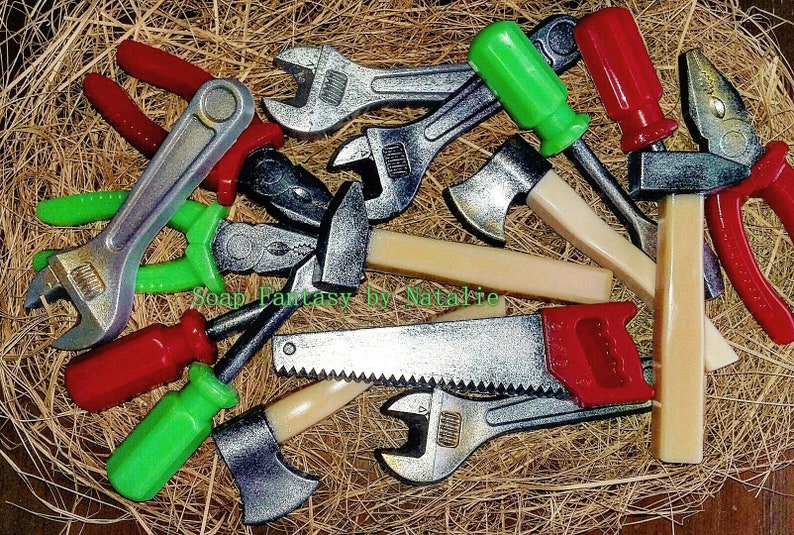 Op de afbeelding: Een verzameling speelgoedgereedschap gemaakt van zeep, waaronder een moersleutel, een tang, een zaag, een hamer, een bijl en schroevendraaiers. De gereedschappen zijn op een strooisel van stro gerangschikt en hebben een realistisch uiterlijk.