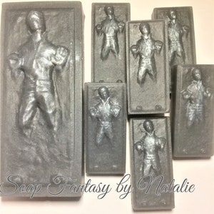 May include: A set of seven gray soap bars shaped like the character Han Solo frozen in carbonite. The bars are different sizes and are arranged in a row. The text "Soap Fantasy by Natalie" is printed on the bottom of the image.
