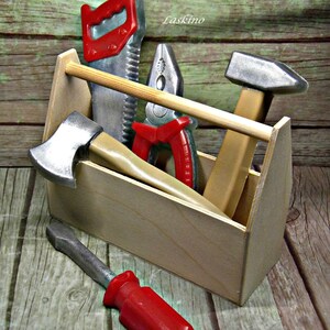 Op de afbeelding: Een houten gereedschapskist gevuld met speelgoedgereedschap, waaronder een zaag, een tang, een hamer, een bijl en een schroevendraaier. De gereedschappen zijn rood en zilver geverfd.