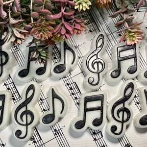 Peut inclure: Une collection d'ornements en forme de notes de musique et de clés de sol blanches avec des contours noirs. Les ornements sont disposés sur une feuille de musique.