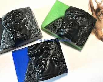 Op de afbeelding: Drie handgemaakte zeepjes met een gorillagezichtontwerp. De zeepjes zijn zwart met een getextureerd oppervlak en liggen op een witte achtergrond. De zeepjes zijn in verschillende kleuren: zwart, groen en blauw.