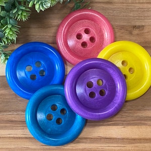May include: Four large, colourful buttons with a four-hole design. The buttons are pink, yellow, blue and purple.