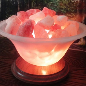 May include: A Himalayan salt lamp with a frosted glass bowl filled with pink Himalayan salt rocks. The lamp is on a wooden base and is lit, casting a warm glow.