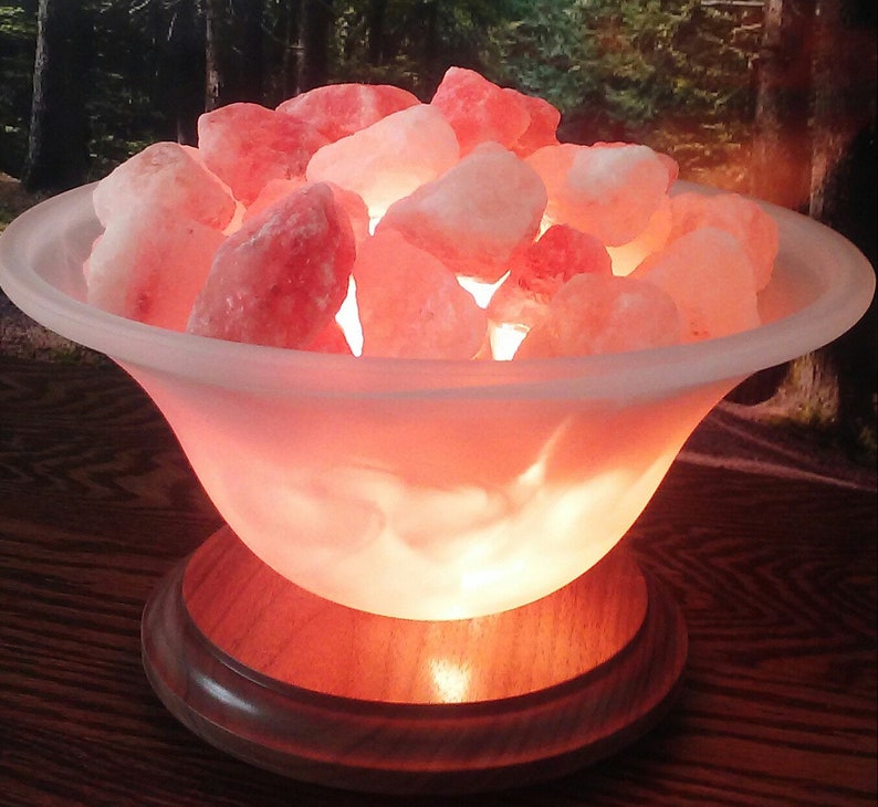 May include: A Himalayan salt lamp with a frosted glass bowl filled with pink Himalayan salt rocks. The lamp is on a wooden base and is lit, casting a warm glow.