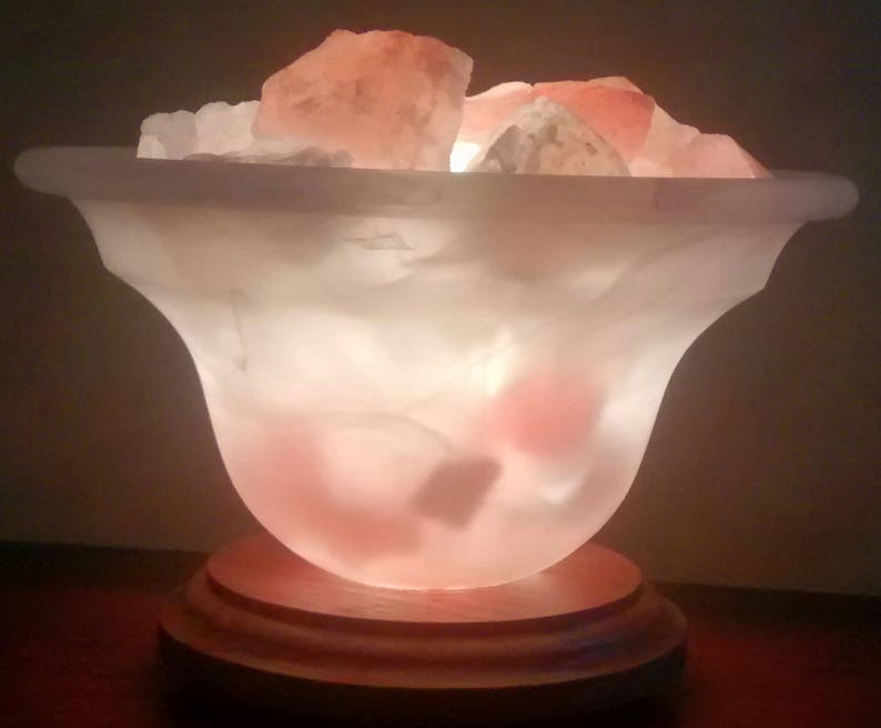 K&ouml;nnte beinhalten: Eine wei&szlig;e Salzlampe mit einem Holzsockel. Die Lampe ist mit rosa Himalaya-Salzkristallen gef&uuml;llt und von innen beleuchtet, wodurch ein warmes Leuchten entsteht.