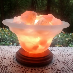 K&ouml;nnte beinhalten: Eine Himalaya-Salzlampe in Form einer Schale mit einem Holzsockel. Die Salzkristalle werden von innen beleuchtet und erzeugen ein warmes orangefarbenes Licht.