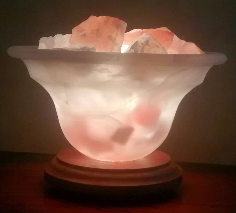 K&ouml;nnte beinhalten: Eine wei&szlig;e Salzlampe mit einem Holzsockel. Die Lampe ist mit rosa Himalaya-Salzkristallen gef&uuml;llt und von innen beleuchtet, wodurch ein warmes Leuchten entsteht.