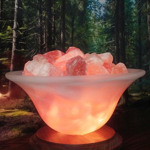 May include: A Himalayan salt lamp with a white frosted glass bowl filled with pink Himalayan salt crystals. The lamp is on a wooden base and is lit, casting a warm glow.