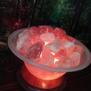 May include: A Himalayan salt lamp with a warm, orange glow. The salt crystals are in a white bowl on a wooden base.