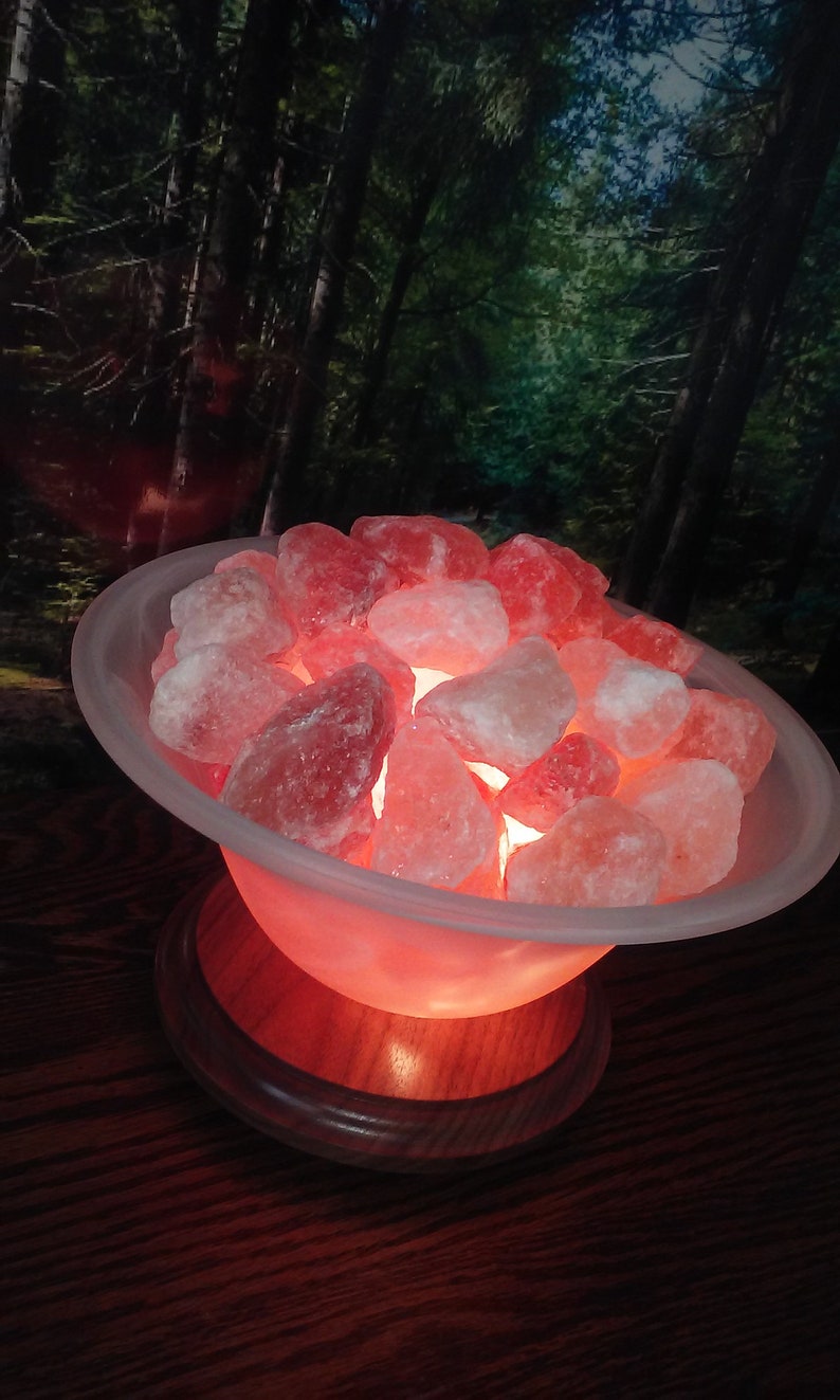 May include: A Himalayan salt lamp with a warm, orange glow. The salt crystals are in a white bowl on a wooden base.