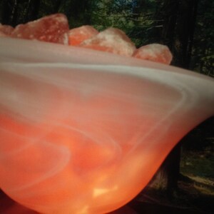 May include: A white, swirling, glass lamp base with a warm, orange glow. The base is filled with pink Himalayan salt rocks.