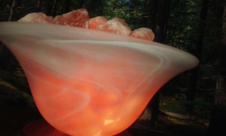 May include: A white, swirling, glass lamp base with a warm, orange glow. The base is filled with pink Himalayan salt rocks.