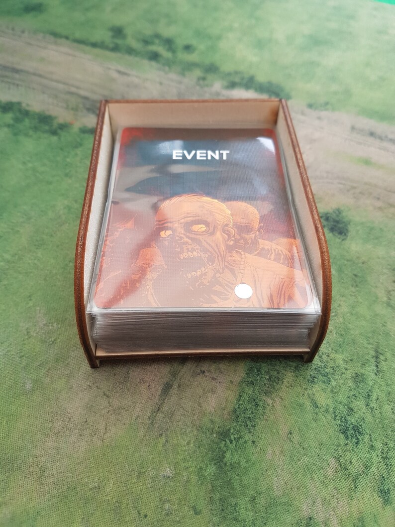 K&ouml;nnte beinhalten: Eine braune Holzkiste mit einem transparenten Kunststoffeinsatz enth&auml;lt einen Stapel Karten. Die oberste Karte zeigt ein Zombiebild und den aufgedruckten Text "EVENT".