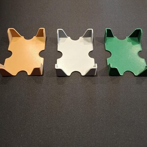 K&ouml;nnte beinhalten: Drei Kartenhalter aus Plastik in verschiedenen Farben: Orange, Wei&szlig; und Gr&uuml;n. Die Halter sind so konzipiert, dass sie ein Kartenspiel aufrecht halten.