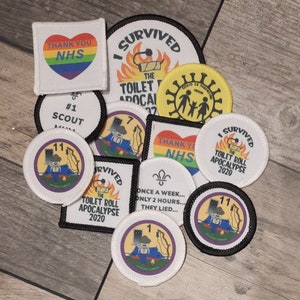 May include: A collection of embroidered badges featuring various designs, including a rainbow heart with the text "Thank You NHS", a toilet roll with flames and the text "I Survived The Toilet Roll Apocalypse 2020", and a cartoon figure with the text "#1 Scout".