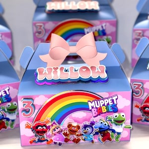 Peut inclure: Une boîte à dragées bleue et rose avec un arc-en-ciel et les mots "Muppet Babies" imprimés dessus. La boîte a un nœud rose et le nom "Willow" imprimé sur le devant. La boîte est décorée de nuages et d'un numéro 3.