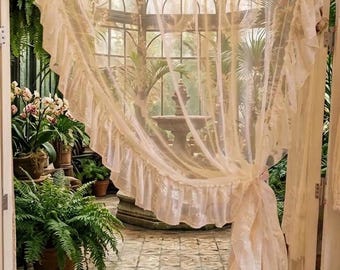 May include: A sheer, off-white curtain panel featuring a delicate, ruffled edge that runs along the side and bottom. The fabric is lightweight and semi-transparent, gathered to one side to create a draped effect that pools slightly on the floor.