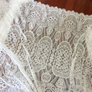 May include: White lace fabric with a delicate floral pattern. The lace has a scalloped edge and is perfect for crafting or sewing projects.