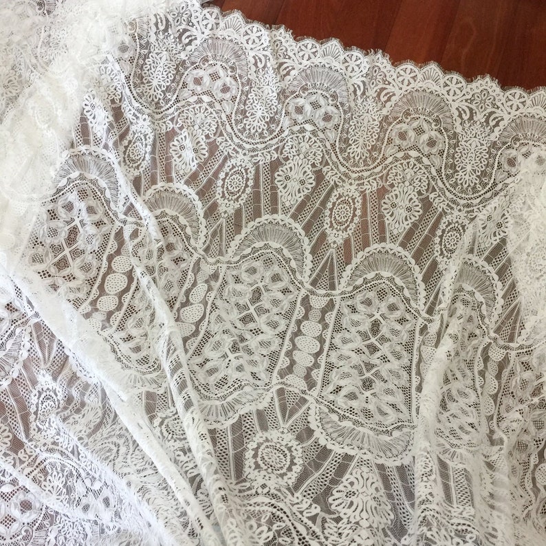 May include: White lace fabric with a delicate floral pattern. The lace has a scalloped edge and is perfect for crafting or sewing projects.