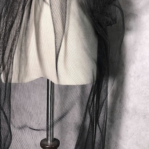 May include: Black sheer fabric with a crinkled texture. The fabric is draped over a white mannequin.