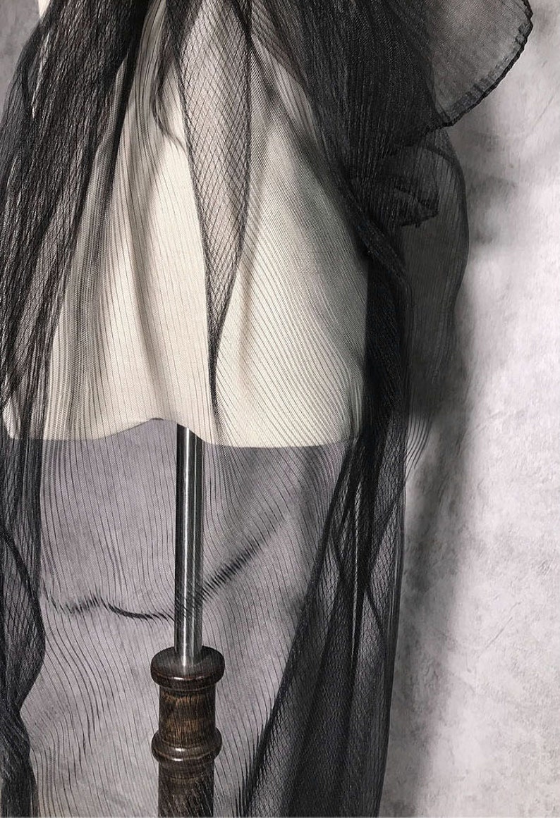 May include: Black sheer fabric with a crinkled texture. The fabric is draped over a white mannequin.