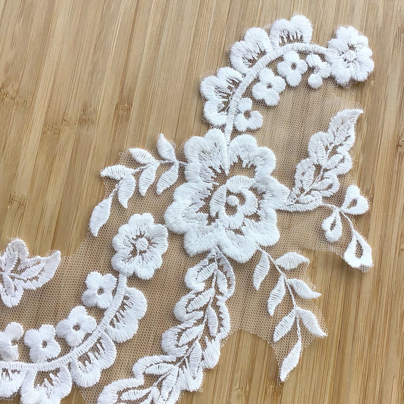 May include: White lace trim with floral embroidery. The lace features delicate flowers and leaves, creating a romantic and elegant design.